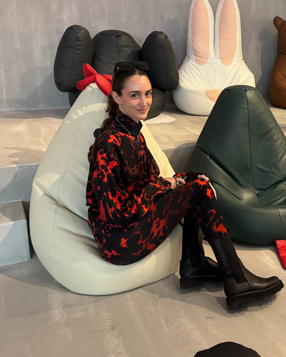Maggie sitting on a cream beanbag in a red and black patterned outfit, smiling at the camera